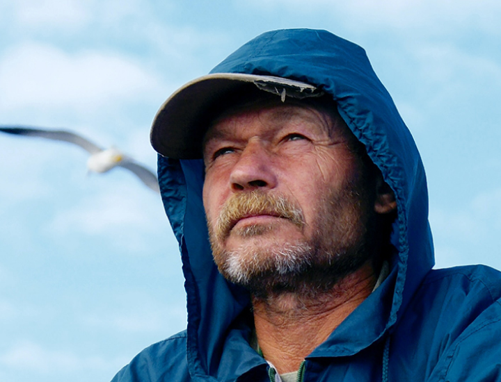 man in a raincoat with a seagull flying overhead