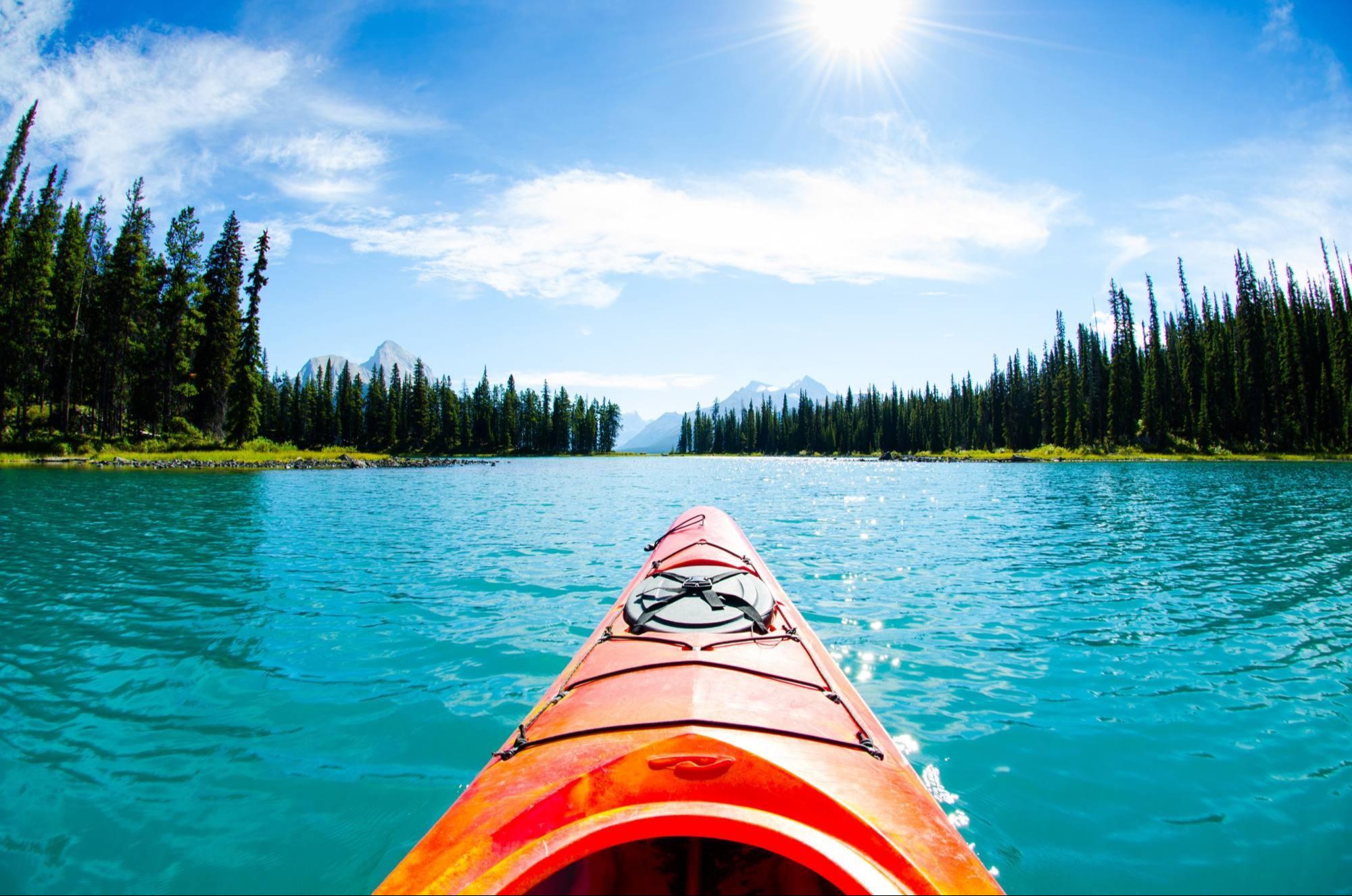 view from the front of kayak in blue water on a sunny day with tall mountains in distance