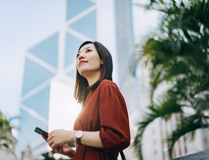 woman next to a modern building holding a cellphone and looking into the distance