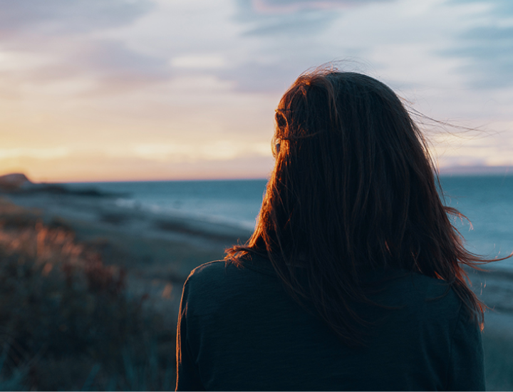 Woman looking out over the beach at sunset.