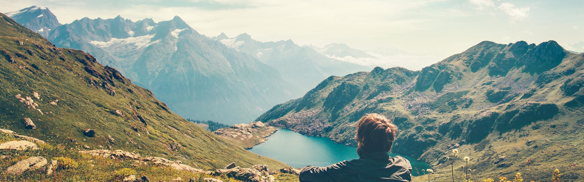 person at the top of a mountain looking at the mountains in the distance and a lake below