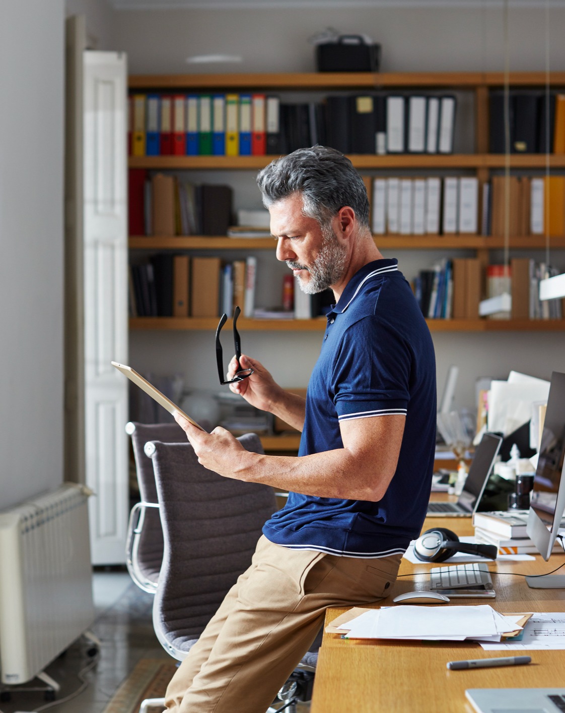 man reading a tablet and leaning on an office desk