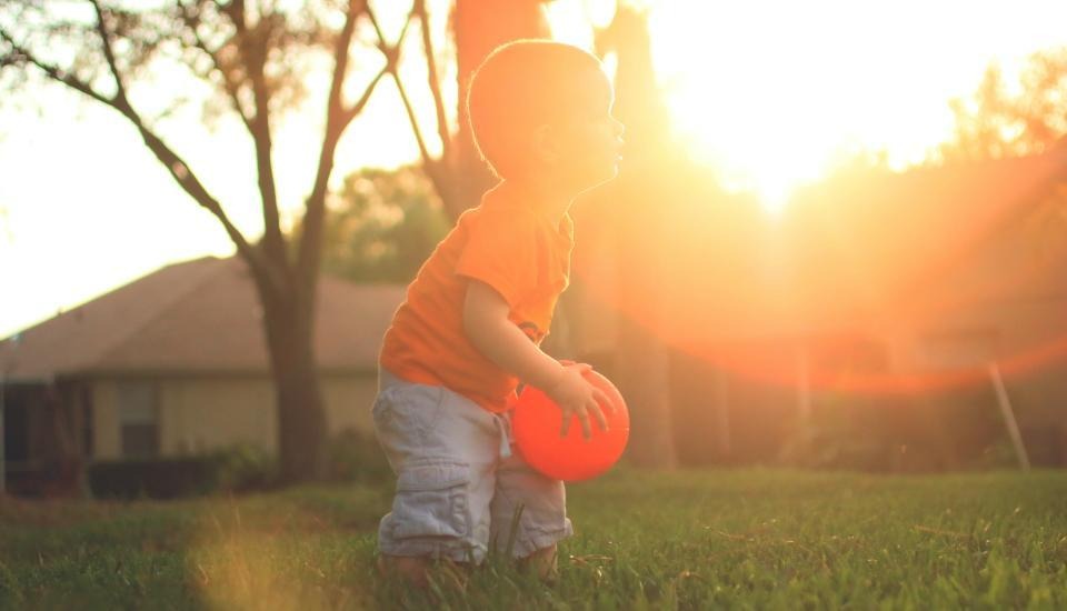 Young child holding a orange ball outside during sunset
