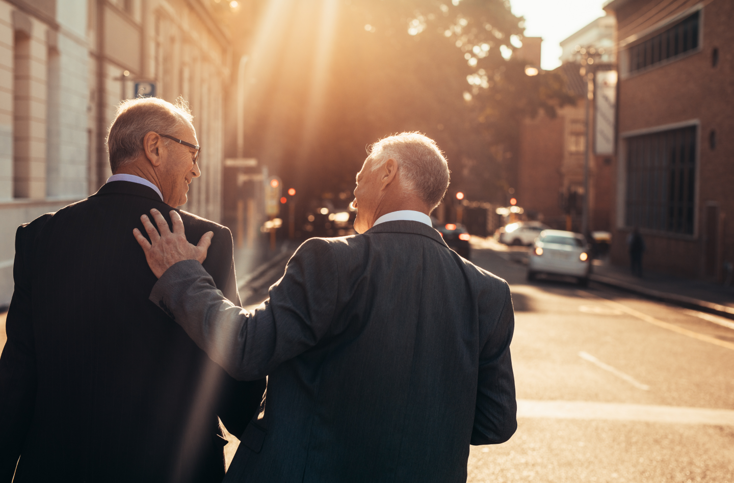 two businessmen walking down a sunny city street and enjoying eachother's company