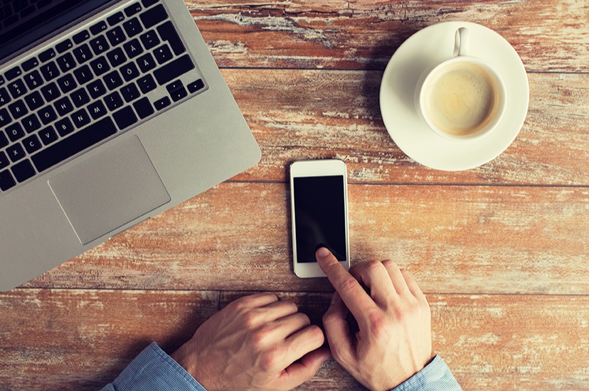 Man checking his iPhone with coffee and laptop