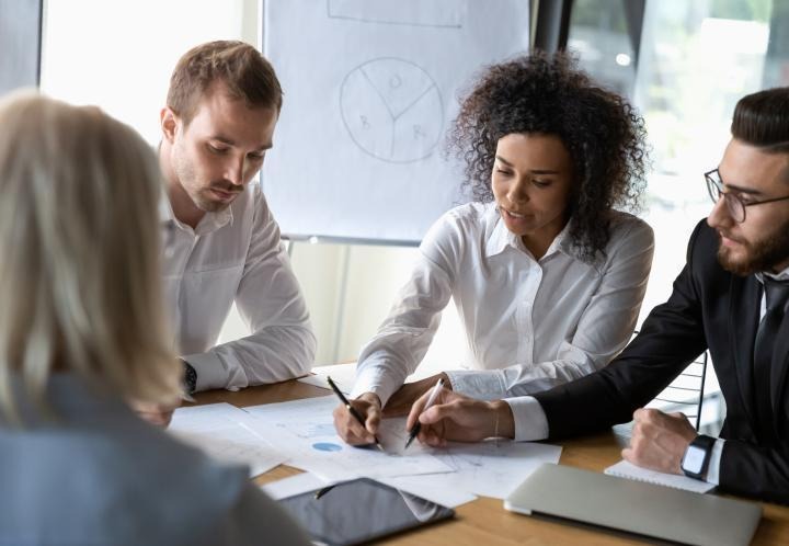 Meeting being held at a table with two people pointing at charts.