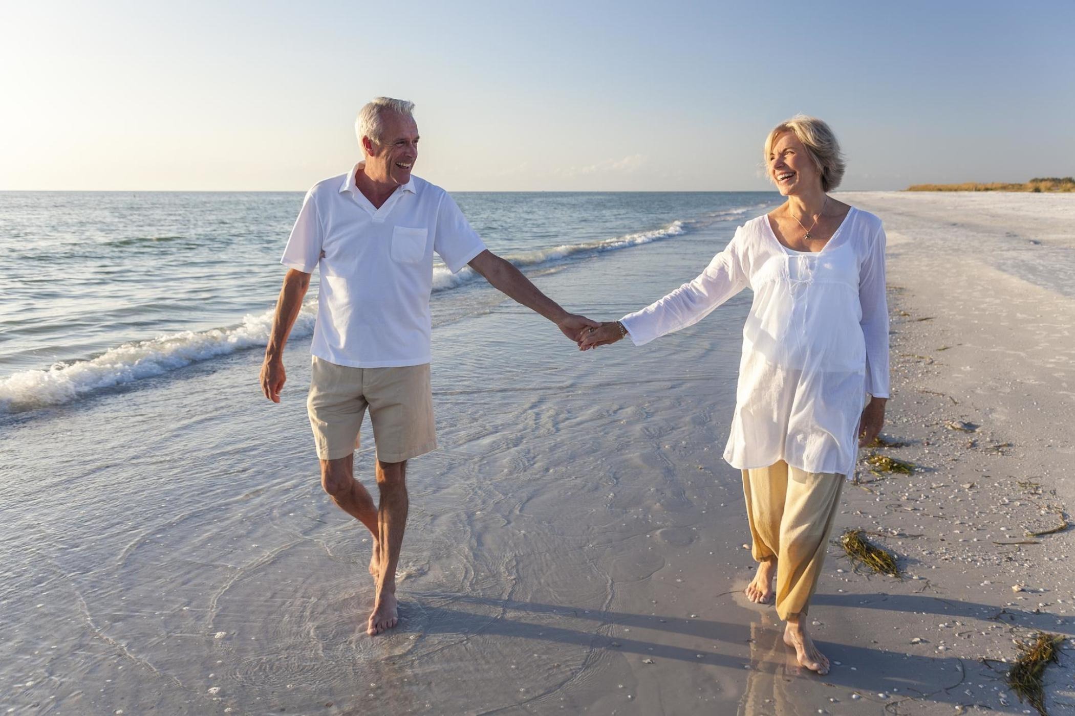 Happy senior couple holding hands and walking on the beach