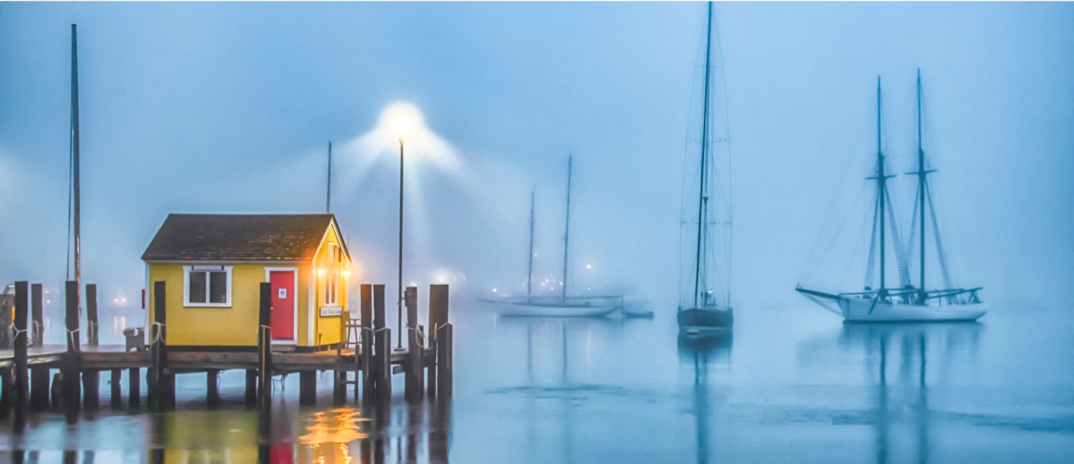 boats with their sails down in a foggy harbor