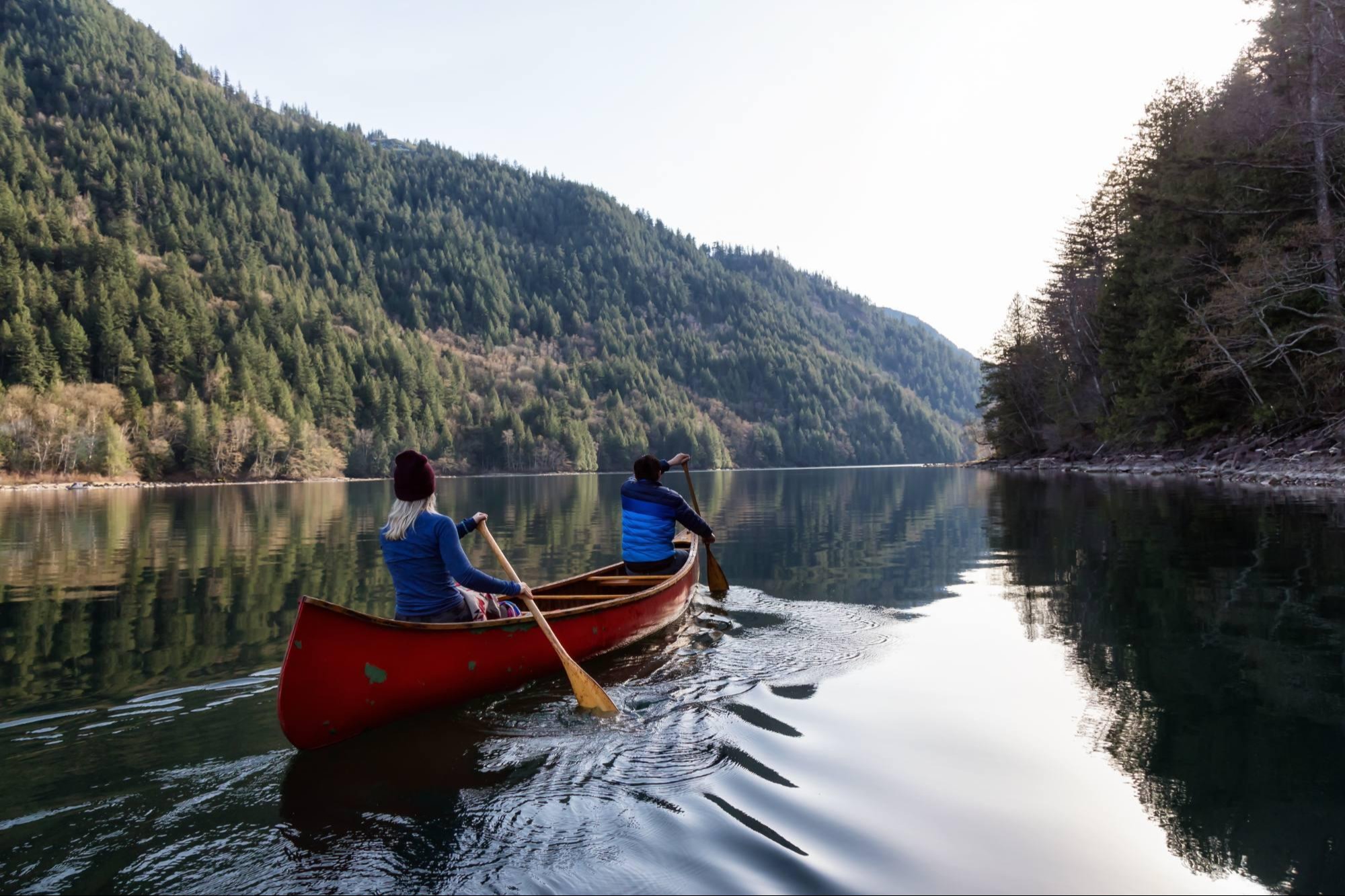 two people canoeing in calm water with forest on both sides