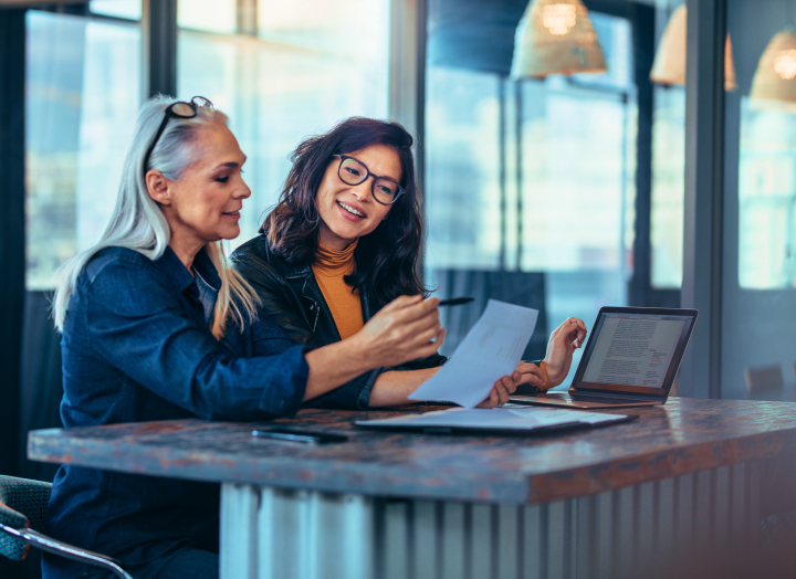 two women looking at a document and one woman using a laptop