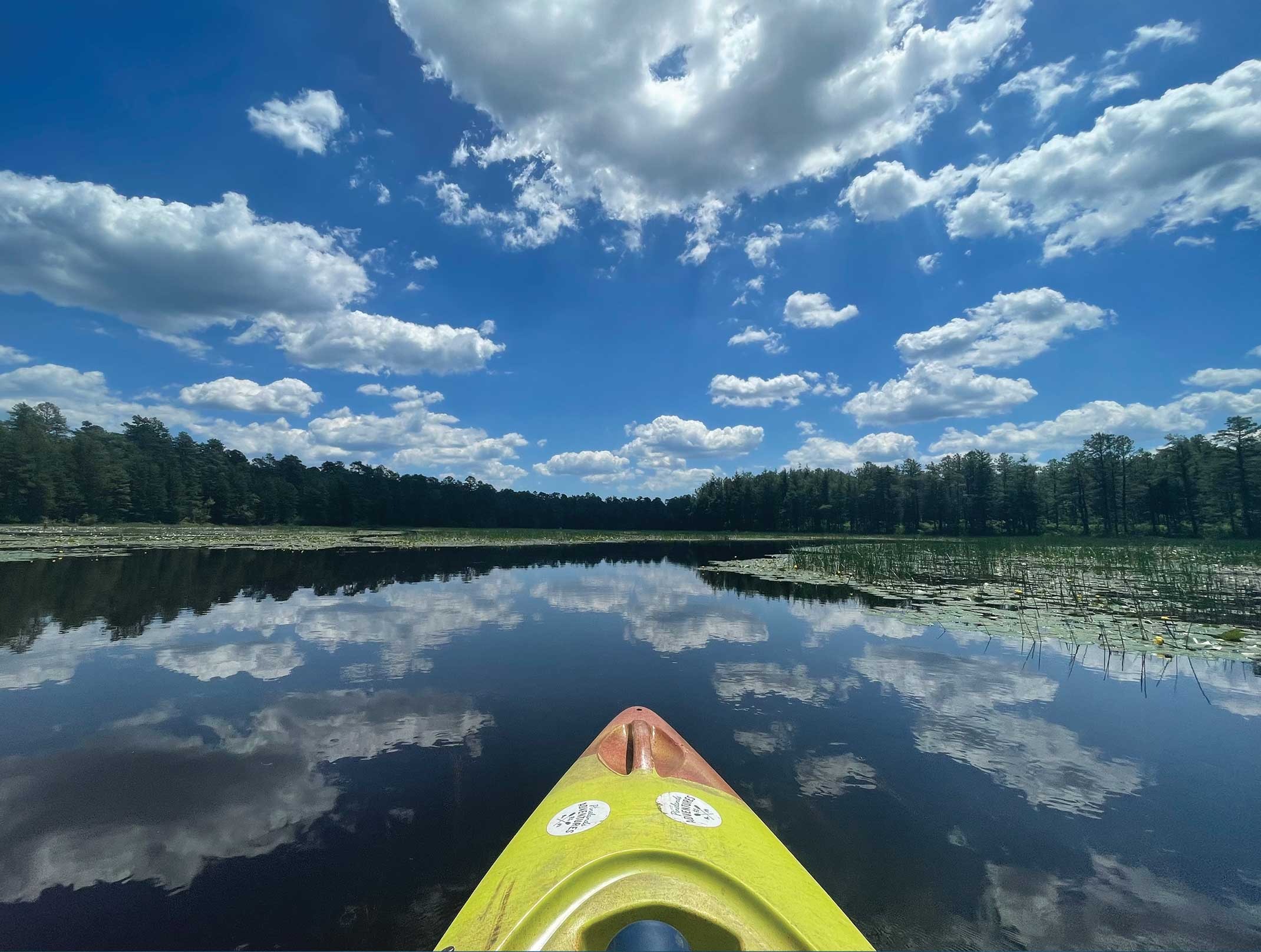 A serene lake reflects a kayak and clouds, creating a tranquil and picturesque outdoor scene.