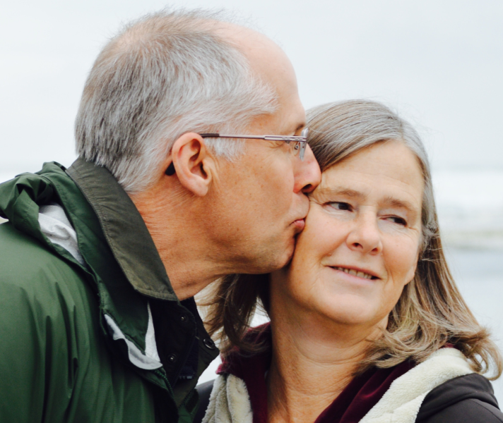 Older man kissing older woman on the beach