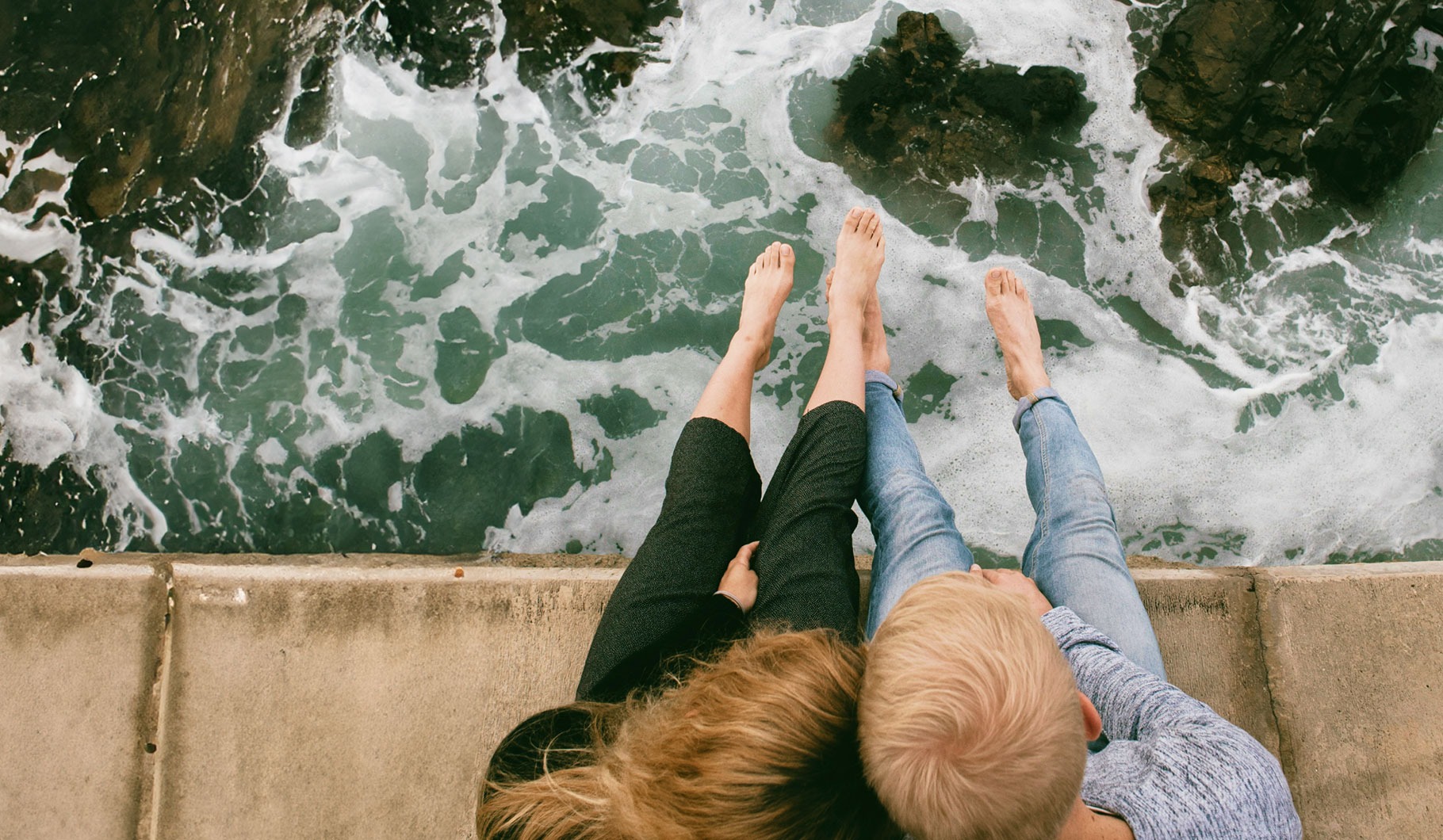 A couple enjoys a peaceful moment on a pier, sitting at the edge and admiring the expansive ocean view.
