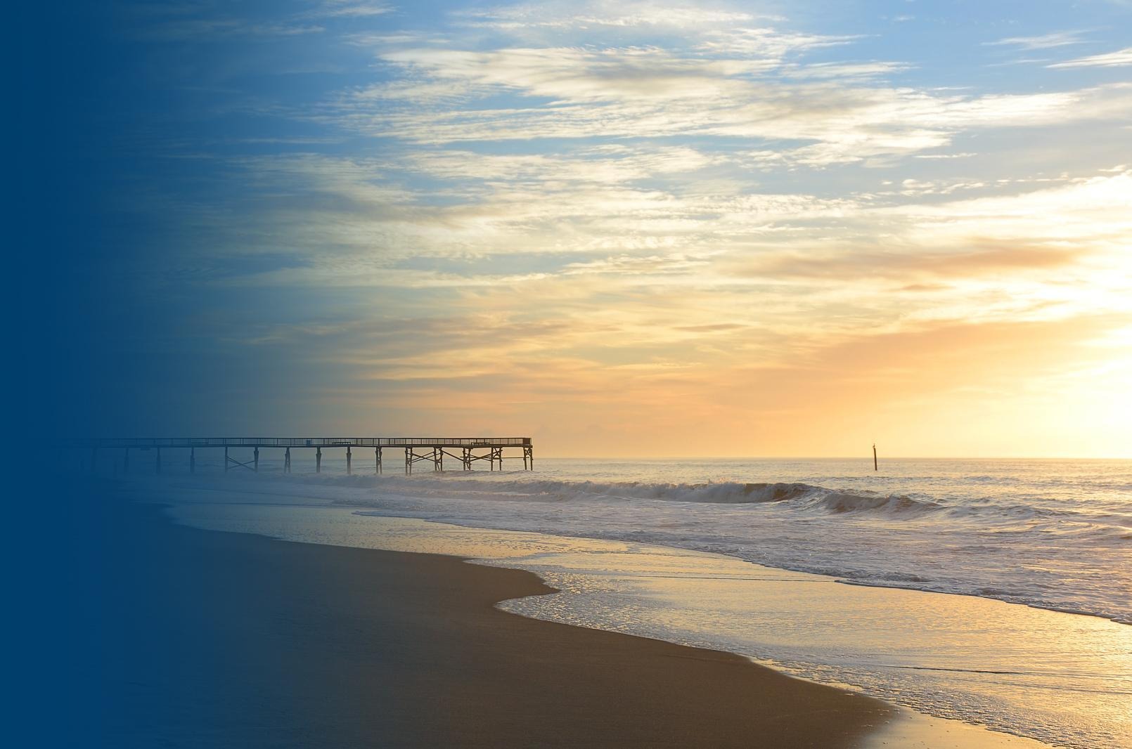 Looking out at sunset over crashing waves on the beach, pier in the background