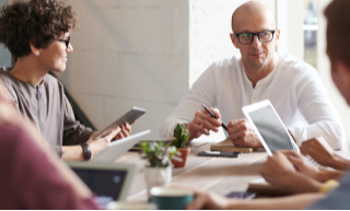 man-with-glasses-meets-with-three-other-people-around-a-table
