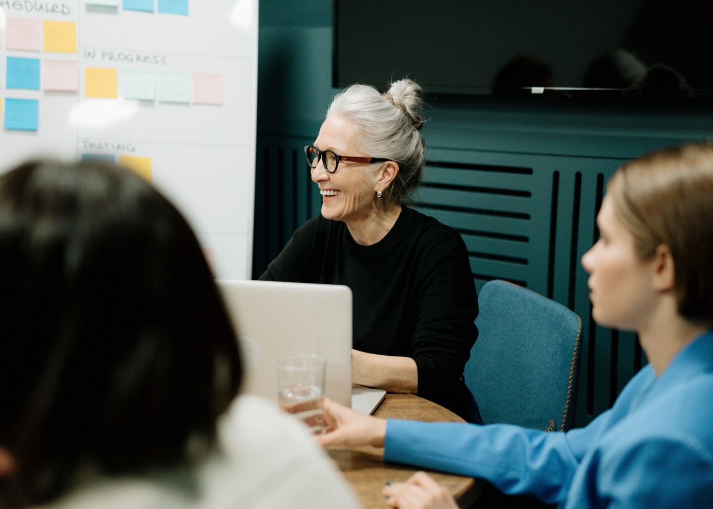 Woman smiling behind a laptop in a meeting room with her coworkers.