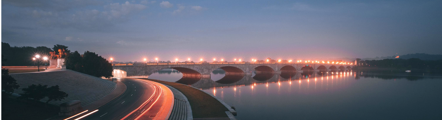 Bridge over still water next to a road with no cars on it at dusk
