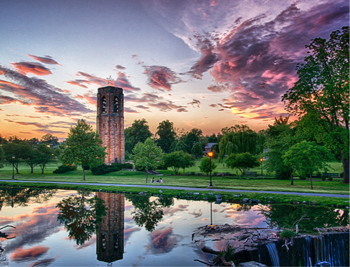 A park with a stone tower and a pond at sunset.