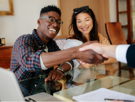 two people shaking hands across a desk while another person looks on