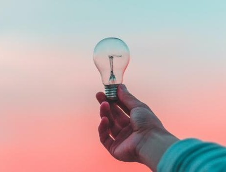 Hand holding lightbulb with pink and blue background