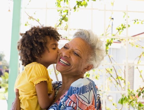 an older woman smiling and laughing while hugging a small child who is kissing her on the cheek