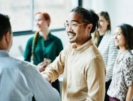 Two people shaking hands in an office, one with their back turned to camera.
