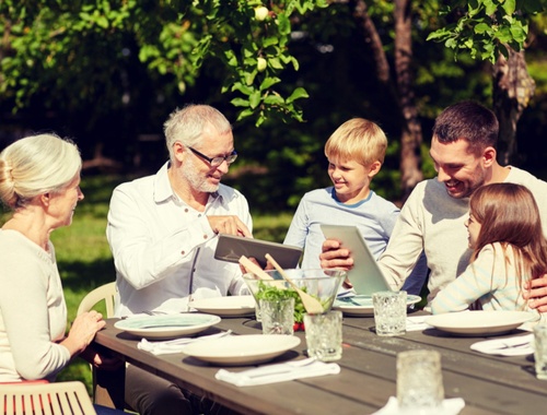 Multi-generational family looking at tablets sitting at a picnic table set for a meal