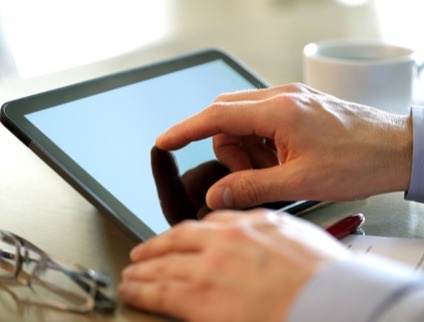 person using a tablet computer and drinking coffee at desk
