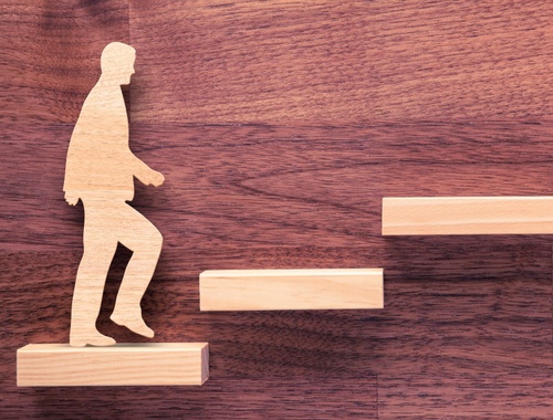 wood cutout of a businessman walking up stairs