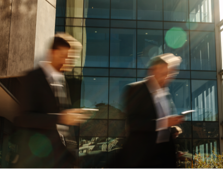 two businessmen looking at their cellphones while walking next to a modern building