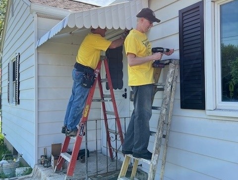 Volunteers working on side paneling of a house